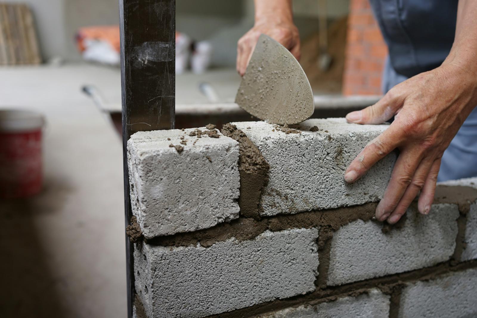 Mains d’un maçon qui étale du mortier à la truelle sur un mur de parpaings en cours de montage