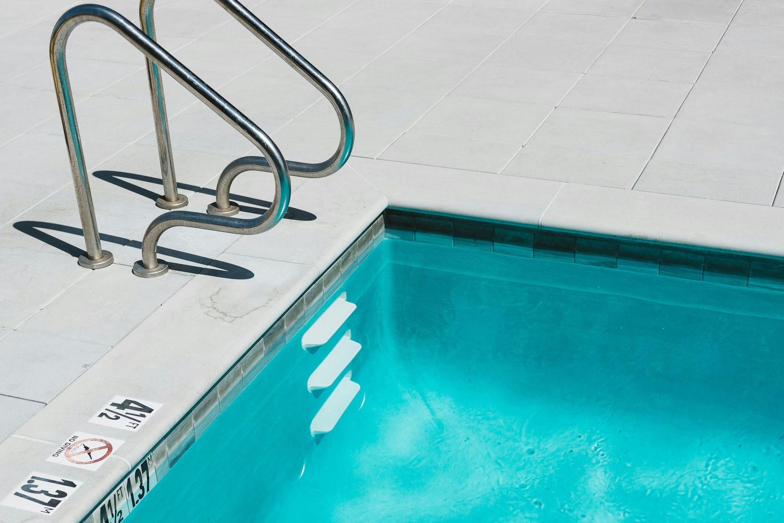 Bord d’une piscine extérieure à l’eau turquoise, avec son échelle en inox, ses marches et ses margelles claires